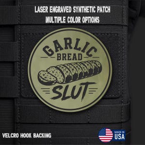 May include: A circular olive green laser-engraved synthetic patch featuring a graphic of a sliced loaf of bread. The text reads GARLIC BREAD SLUT. The patch includes a Velcro hook backing and is displayed on a black tactical gear surface.