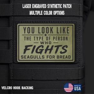 May include: A rectangular olive green synthetic patch with black laser-engraved text that reads: YOU LOOK LIKE THE TYPE OF PERSON WHO FIGHTS SEAGULLS FOR BREAD. The patch features a hook backing and is attached to a black tactical gear surface.