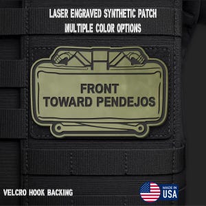 May include: A rectangular olive green synthetic patch with black laser-engraved text reading FRONT TOWARD PENDEJOS. The patch features a stylized graphic of two pistols and has a hook backing. Text above reads LASER ENGRAVED SYNTHETIC PATCH MULTIPLE COLOR OPTIONS and VELCRO HOOK BACKING.