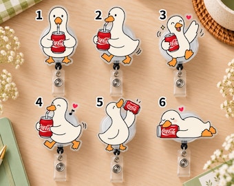 Könnte beinhalten: Sechs Ausweishalter aus Acryl mit weißen Cartoon-Enten mit orangefarbenen Schnäbeln und Füßen. Jede Ente interagiert mit einer roten Coca-Cola-Dose und zeigt verschiedene Posen wie Trinken mit Strohhalm oder Ausruhen.
