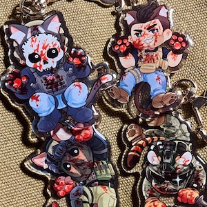 May include: Four acrylic keychains featuring chibi-style characters in tactical gear with cat ears and tails. The characters are splattered with red paint, wearing vests, helmets, and masks. Each keychain includes a gold-toned metal lobster clasp.