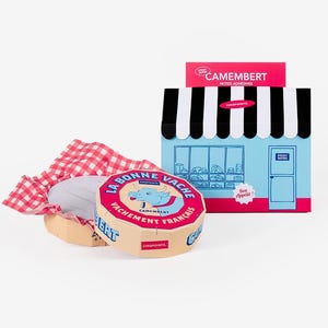 Peut inclure: Un produit de fromage Camembert avec une étiquette rouge et bleue, un tissu à carreaux rouges et blancs et une boîte en forme de devanture bleue et blanche. L'étiquette du fromage indique "La Bonne Vache" et "Vachement Francais".