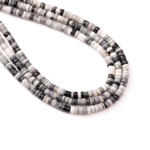 May include: Strands of small, round beads in shades of gray, white, and black. The beads are strung together, forming multiple necklaces. The beads have a flat, disc-like shape. The background is white.