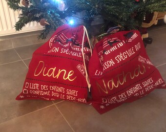 May include: Two red Christmas gift bags with white drawstring closures. The bags are decorated with gold lettering that reads "Service Exp. Special Season for Diane" and "Service Exp. Special Season for Natha".