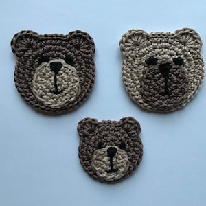 Può includere: Tre volti di orso all'uncinetto di diverse dimensioni. Gli orsi hanno occhi e nasi neri.