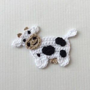 May include: A crocheted white cow with black spots and a brown face. The cow is a small, flat applique.