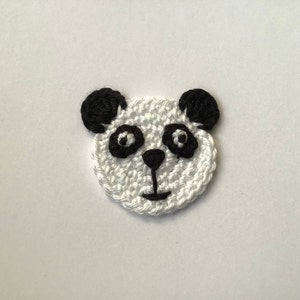 Peut inclure: Un visage de panda en crochet blanc avec des oreilles, des yeux, un nez et une bouche noirs.
