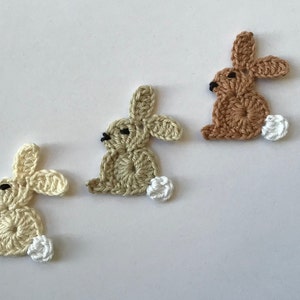 Peut inclure: Trois formes de lapin en crochet avec des queues blanches et duveteuses. Les lapins sont beige, brun clair et brun.