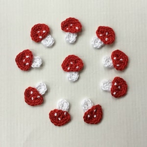 Op de afbeelding: Tien gehaakte paddenstoelversieringen in rood en wit. De paddenstoelen zijn klein en hebben een witte steel en een rode dop met witte stippen.