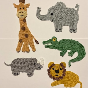 Könnte beinhalten: Fünf gehäkelte Tier-Applikationen: eine Giraffe, ein Elefant, ein Krokodil, ein Nashorn und ein Löwe. Die Giraffe ist braun und orange, der Elefant ist grau, das Krokodil ist grün, das Nashorn ist grau und der Löwe ist gelb und braun.