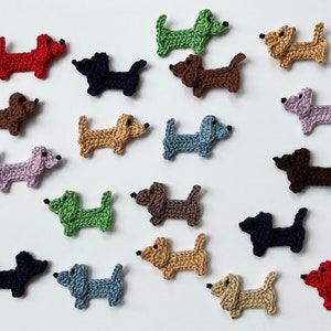 Może przedstawiać: Kolekcja 18 szydełkowych ozdób w kształcie psa rasy dachshund w różnych kolorach, w tym czerwonym, niebieskim, zielonym, brązowym i beżowym.