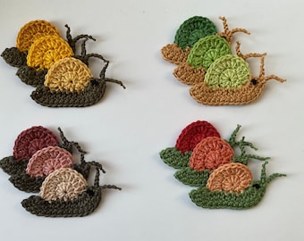 May include: Three sets of crocheted snails, each set with three snails in different shades of green, yellow, and red. The snails are made with a variety of stitches and textures, and they have a charming, whimsical look.