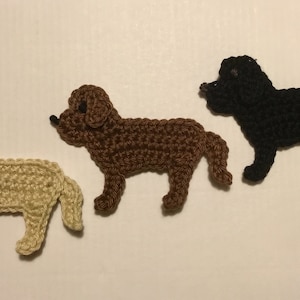 Könnte beinhalten: Drei gehäkelte Hundefiguren. Die Hunde sind braun, schwarz und cremefarben. Die Hunde sitzen alle mit eingerolltem Schwanz.