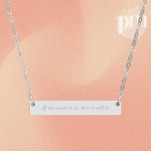 May include: A silver bar necklace with a delicate chain. The rectangular pendant is engraved with the phrase "If it's meant to be, then it will be." The background is a soft peach color.