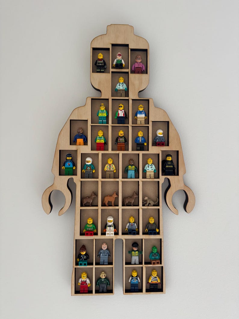 May include: A light-colored wooden wall-mounted display shelf shaped like a toy figure. The shelf features multiple rectangular compartments containing various small plastic toy figures, including people and animals, arranged in rows within the frame.