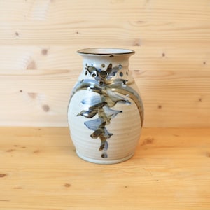 May include: A handmade ceramic vase with a cream base and a flared rim. The vase has a distinctive design with brown and blue abstract patterns. It stands at approximately 25 cm in height.