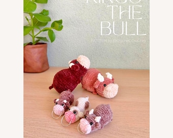 May include: Four crocheted bull amigurumi toys. Two are red, one is brown and white, and one is brown. The larger bulls are lying down, and the smaller bulls are standing. The text "RINGO THE BULL" and "NO SEW" are visible in the image.