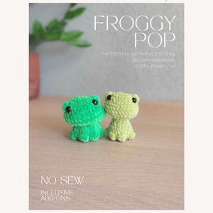 May include: Two crocheted frog plushies, one green and one light green, sitting on a wooden surface. The text "FROGGY POP" is above the frogs, and the text "NO-SEW INCLUSIVE ADD-ONS" is below the frogs.