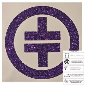 May include: A purple glitter iron-on transfer with a cross symbol inside a circle. Suitable for home ironing on cotton and polyester blends. Application instructions are provided. The design is sparkly.