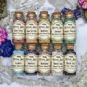 May include: A collection of twelve small glass bottles filled with colorful ritual salts. Each bottle has a cork stopper and a label with the words "Ritual Salt" and a specific intention, such as "Love Spell" or "Clarity". The salts are infused with various herbs and crystals.