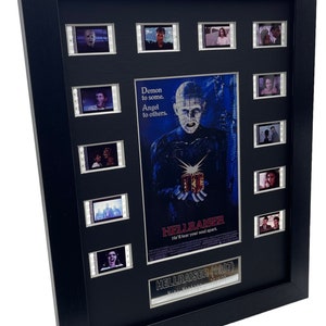 Może przedstawiać: Oprawiony plakat filmowy do filmu grozy "Hellraiser" z 1987 roku, z czarną ramą i srebrną tabliczką. Plakat przedstawia postać z haczykowatą, metalową twarzą i tekstem "Demon to some. Angel to others. He'll tear your soul apart." Rama zawiera 10 pasków z kliszami filmowymi ze scenami z filmu.