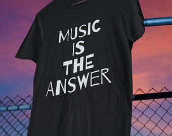 May include: Black t-shirt with the white text "MUSIC IS THE ANSWER". The shirt is hanging on a metal bar against a backdrop of a sunset and a chain-link fence. The t-shirt is a classic crew neck style.