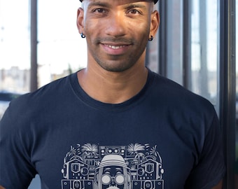 May include: A person wearing a navy blue t-shirt and a black cap. The t-shirt features a white graphic of a person with sunglasses and speakers, with the text "JUNGLIST SOUND" below. The cap has a green brim.