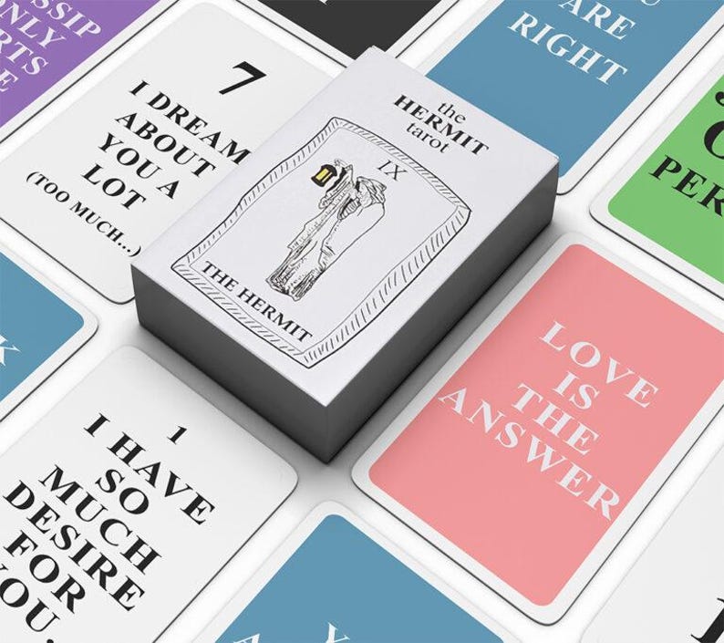 Op de afbeelding: Een pak tarotkaarten met verschillende berichten en illustraties. De bovenste kaart leest "The Hermit" met een zwart-wit illustratie. Andere kaarten tonen zinnen als "Love is the Answer" en "I have so much desire for you."