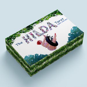 May include: A tarot deck box with the title "The Hilda Tarot" in floral letters. The image features a woman in a polka dot bikini swinging on a tire swing. Green foliage frames the top and sides of the box.