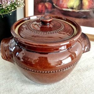 Könnte beinhalten: Ein brauner Keramiktopf mit Deckel und einem Knopf oben. Der Topf hat eine Perlenverzierung am Rand und eine glänzende Oberfläche.