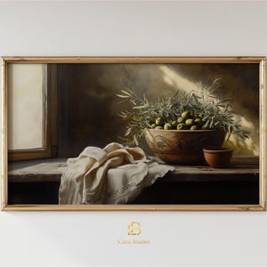 Pode incluir: Pintura emoldurada de natureza morta com uma tigela de madeira cheia de azeitonas verdes e ramos de oliveira. Uma pequena tigela de terracota está ao lado. Um pano dobrado e uma janela também são visíveis. A pintura tem uma paleta de cores quentes e terrosas.