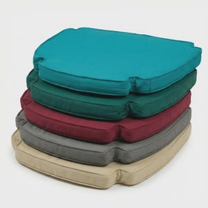 Peut inclure: Une pile de cinq coussins de siège d'extérieur de différentes couleurs. Le coussin supérieur est turquoise, suivi de vert, bordeaux, gris et beige. Chaque coussin a une forme arrondie avec une légère indentation sur les côtés.