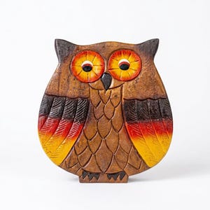 May include: A carved wooden owl figurine featuring a dark brown body with textured feather details. The owl has large, circular eyes painted in bright orange and yellow, and the wing tips are accented with a gradient of red, orange, and yellow.