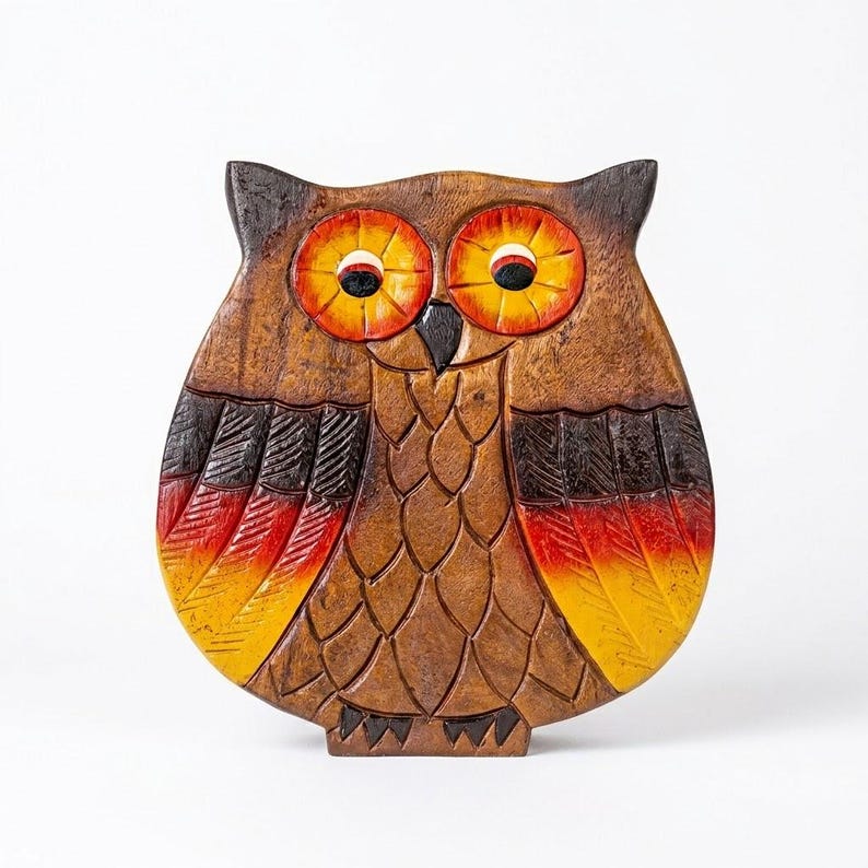 May include: A carved wooden owl figurine featuring a dark brown body with textured feather details. The owl has large, circular eyes painted in bright orange and yellow, and the wing tips are accented with a gradient of red, orange, and yellow.