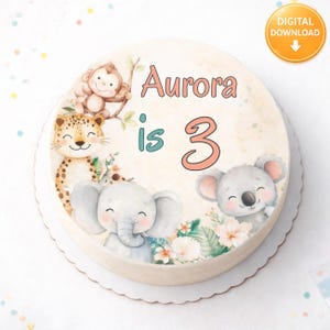 Può includere: Una torta rotonda decorata con animali dei cartoni animati, tra cui una scimmia, un leopardo, un elefante e un koala. La torta ha la scritta "Aurora compie 3 anni" in rosa e verde acqua. La torta è su un piatto bianco con bordo smerlato.