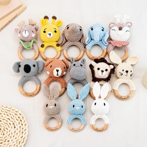 Puede incluir: Una colección de sonajeros para bebés hechos a mano con ganchillo, con formas de animales como una jirafa, un elefante y un koala. Cada sonajero tiene un anillo de madera y está hecho en colores pastel suaves. Algunos sonajeros tienen nombres grabados.