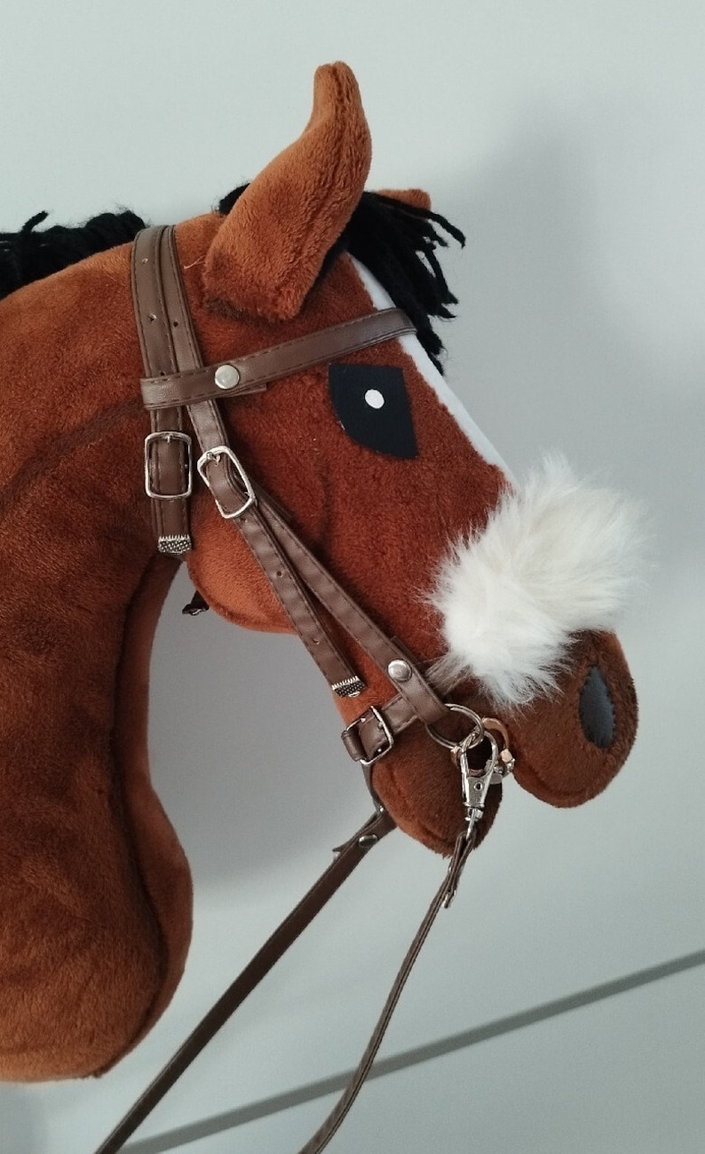 May include: Brown and white plush rocking horse with a black mane and tail. The horse has a brown leather bridle with a silver buckle and a white fur patch on its nose.