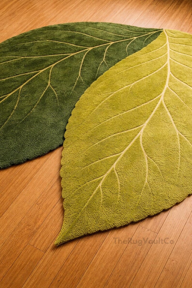 May include: Two leaf-shaped rugs in shades of green. The rugs have a textured surface and detailed vein patterns in a lighter green color. The rugs are placed on a wooden floor.