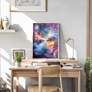 May include: A framed art print depicting a vibrant, colorful nebula with planets and swirling galaxies. The artwork features shades of blue, purple, orange, and green. The print is displayed on a wooden desk with a small lamp and a potted plant.