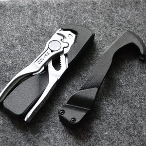 May include: A silver multi-tool with a black handle and the text "99-100" printed on it. A black tool with a hook-like shape is also pictured.