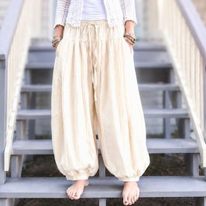 Può includere: Un cardigan bianco a maniche lunghe all'uncinetto con scollo rotondo indossato sopra una canotta bianca semplice, abbinato a pantaloni alla turca color crema, ampi, con vita elasticizzata con coulisse e polsini arricciati alle caviglie.