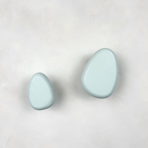 May include: Two light blue wooden knobs shaped like pebbles. The knobs are smooth and have a slightly textured surface.