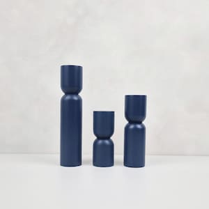 Puede incluir: Tres candelabros azules de diferentes alturas. Los candelabros son de madera y tienen un acabado liso y mate.