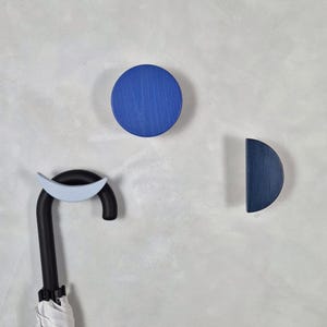 Può includere: Un moderno portaombrelli a parete con un gancio curvo nero e un accento azzurro. L'immagine mostra anche un gancio a parete circolare blu e un gancio a parete a semicerchio blu. L'ombrello è bianco e nero.
