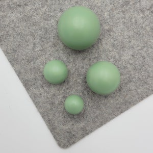 May include: Four green round ornaments of various sizes on a gray felt background.