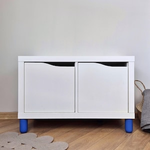 May include: White two-drawer storage cabinet with blue legs. The cabinet has two drawers with curved edges and a white top.