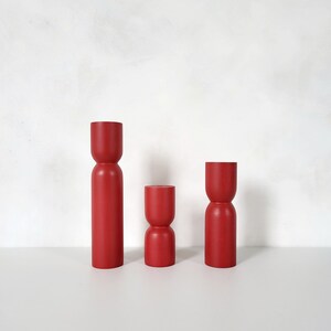 Puede incluir: Tres candelabros de madera rojos de diferentes alturas. Los candelabros son cilíndricos con una ligera forma de reloj de arena.