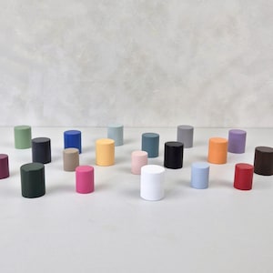 以下が含まれることがあります： 緑、青、黄色、ピンク、黒、白など、さまざまな色の小さな円筒形の木製オブジェクトのコレクション。オブジェクトは、ニュートラルな背景に対して白い表面に配置されています。