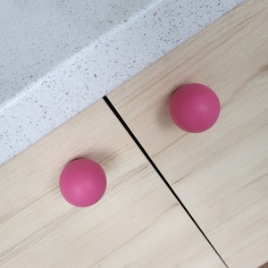 May include: Two pink round cabinet knobs on a light wood surface.