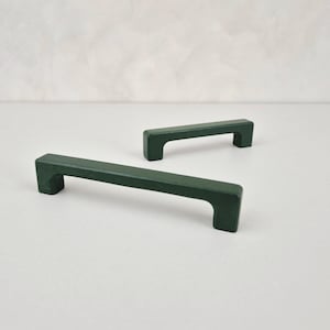 May include: Two dark green cabinet pulls with a rectangular shape and a cutout handle. The pulls are made of wood and have a matte finish.